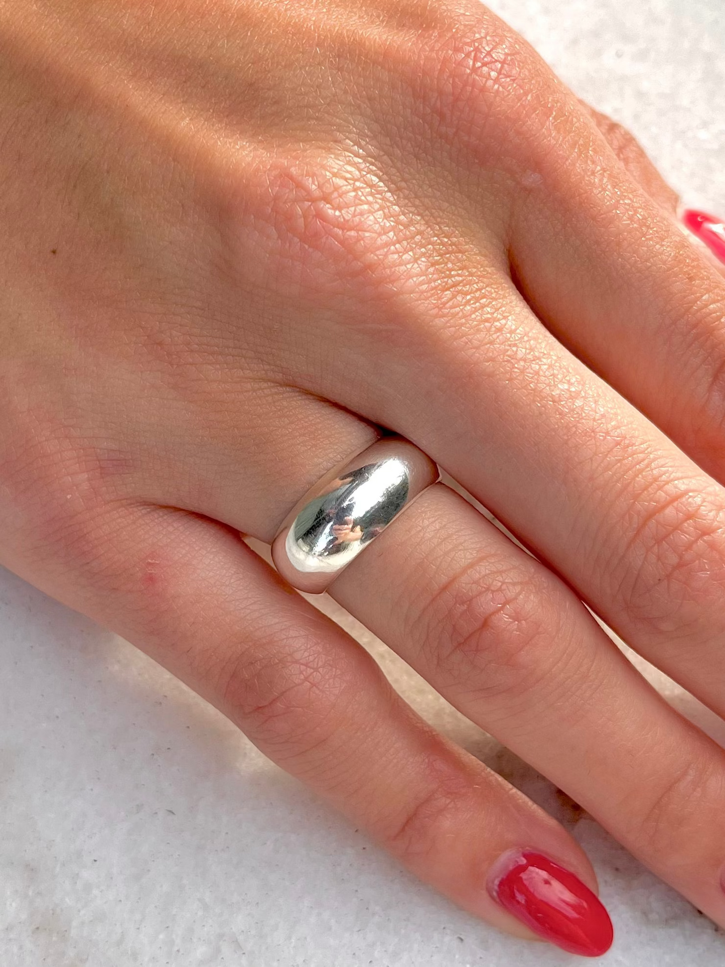 Hand with red nail polish wearing a silver ring on a white surface