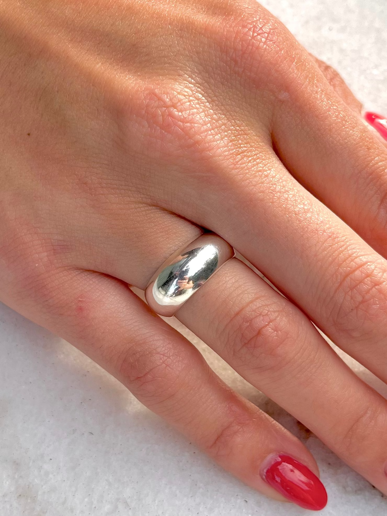 Hand with red nail polish wearing a silver ring on a white surface